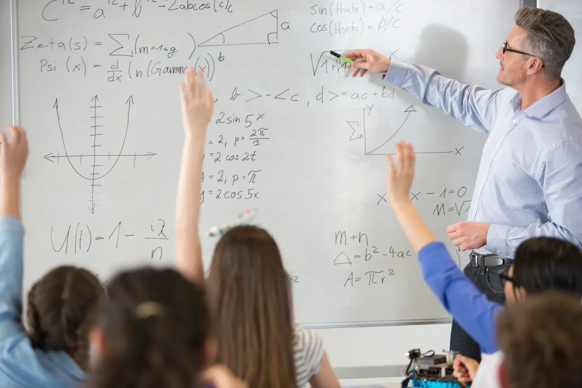 A group of students are raising their hands to answer a question on a whiteboard