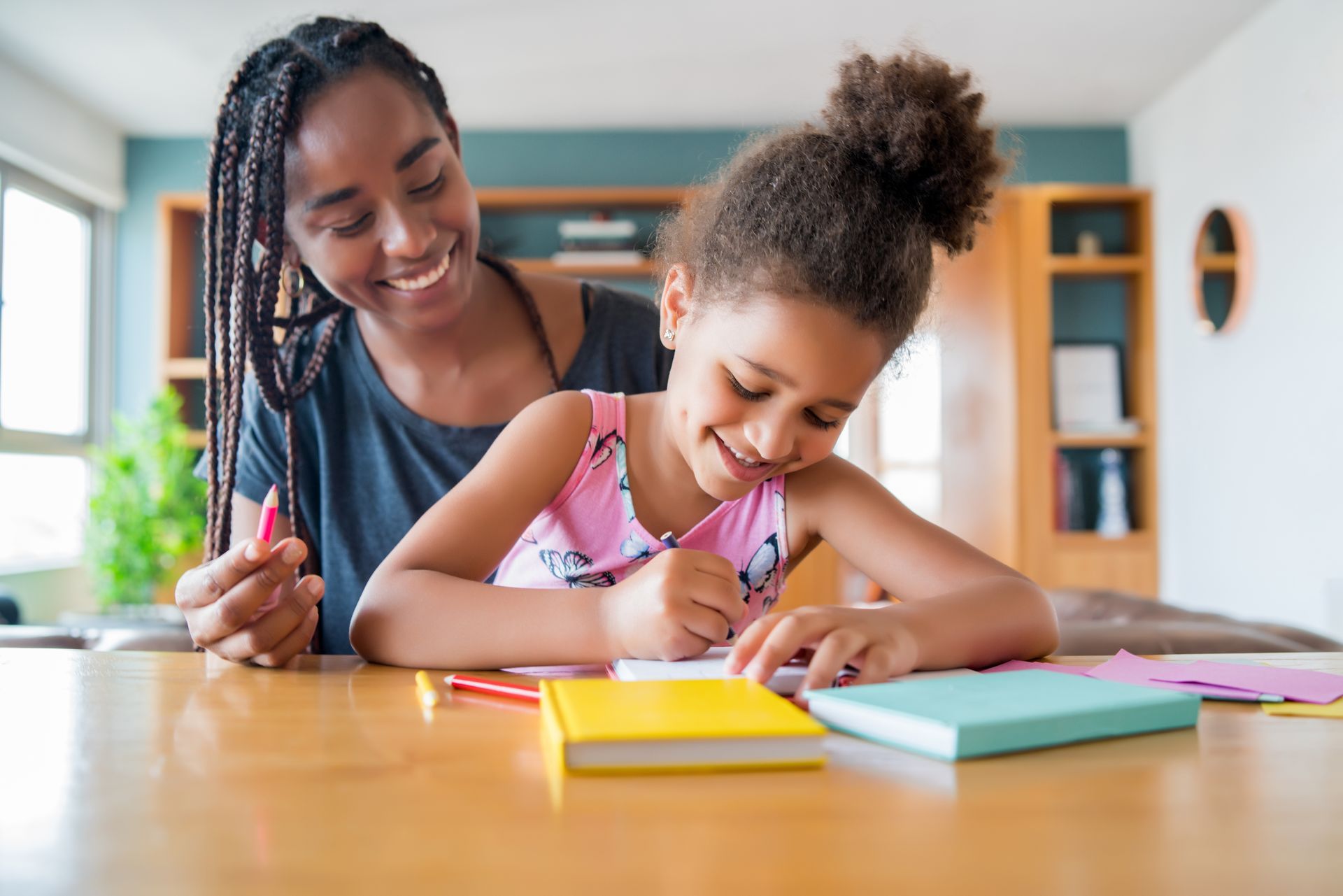 A woman is helping a little girl with her homework at a table.