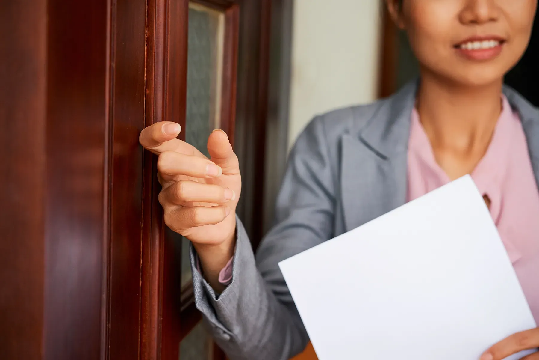 A woman is holding a piece of paper and knocking on a door.
