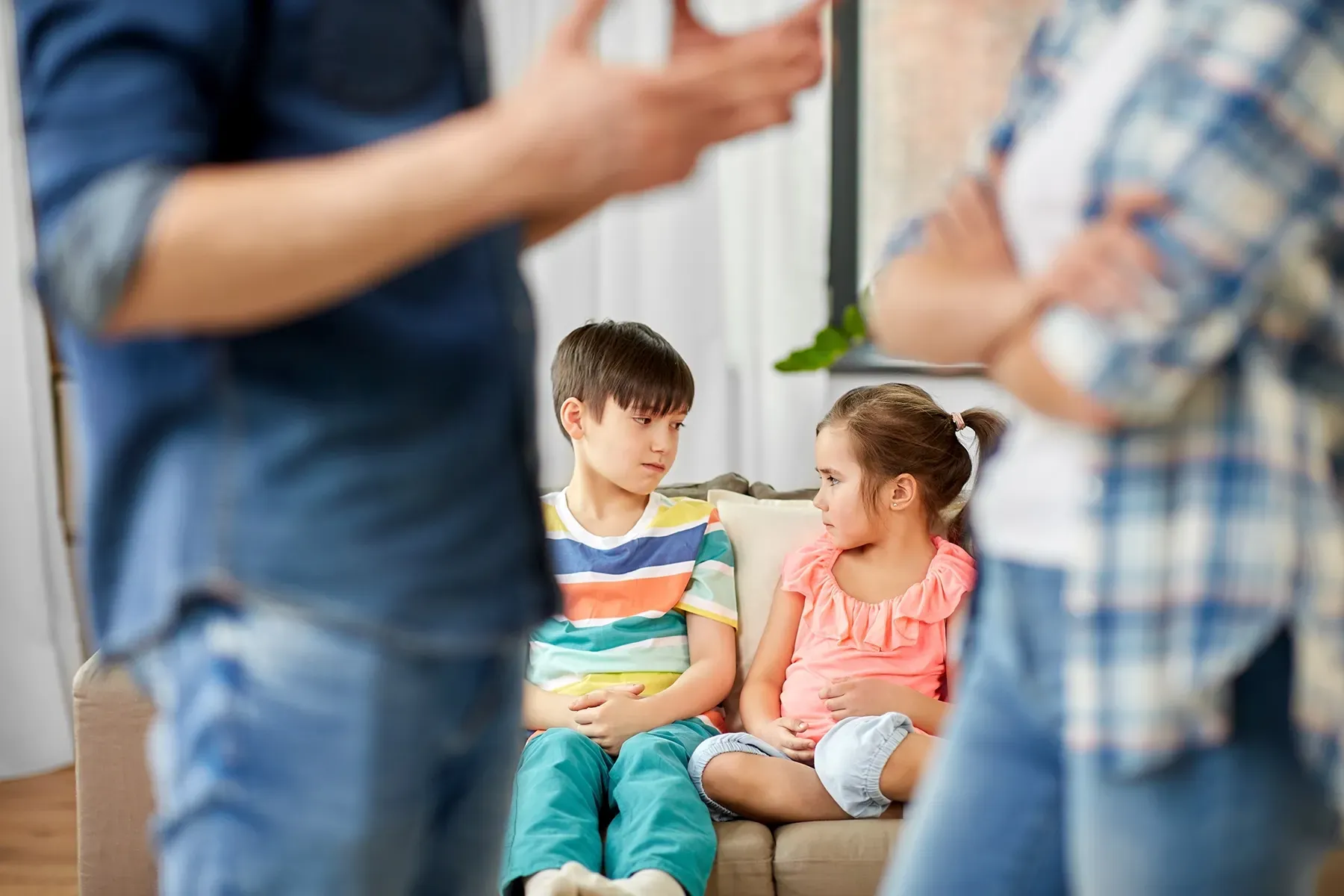 a pair of children on a couch watching their parents argue