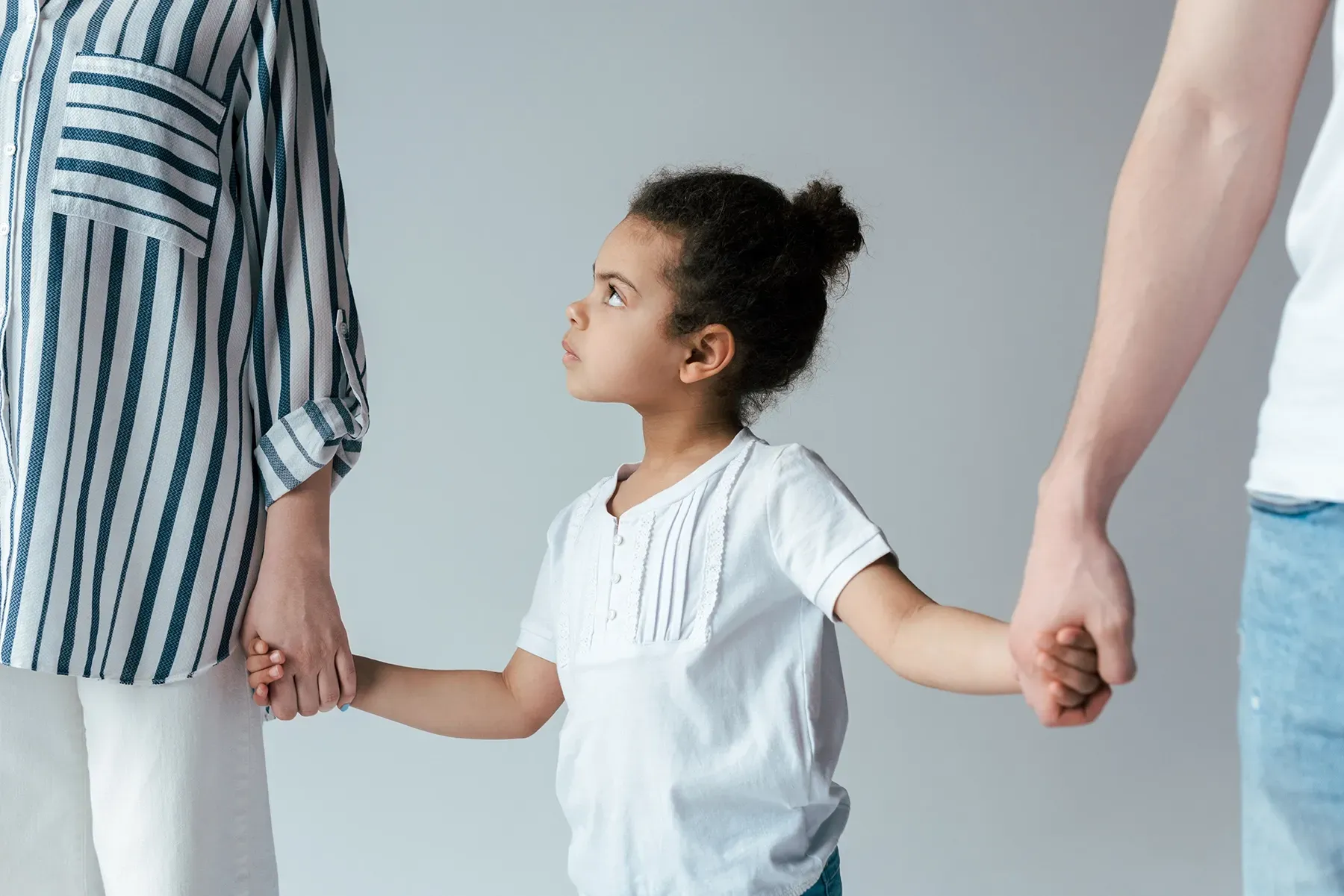 A little girl is holding hands with her parents.