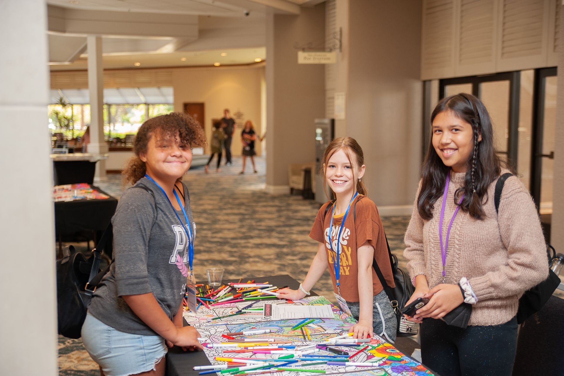 Three young girls are standing around a table filled with markers.