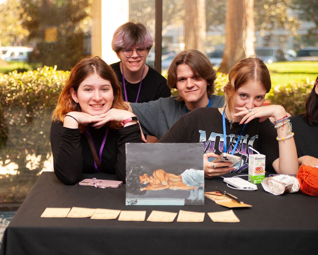 A group of young people are sitting at a table with a painting on it.