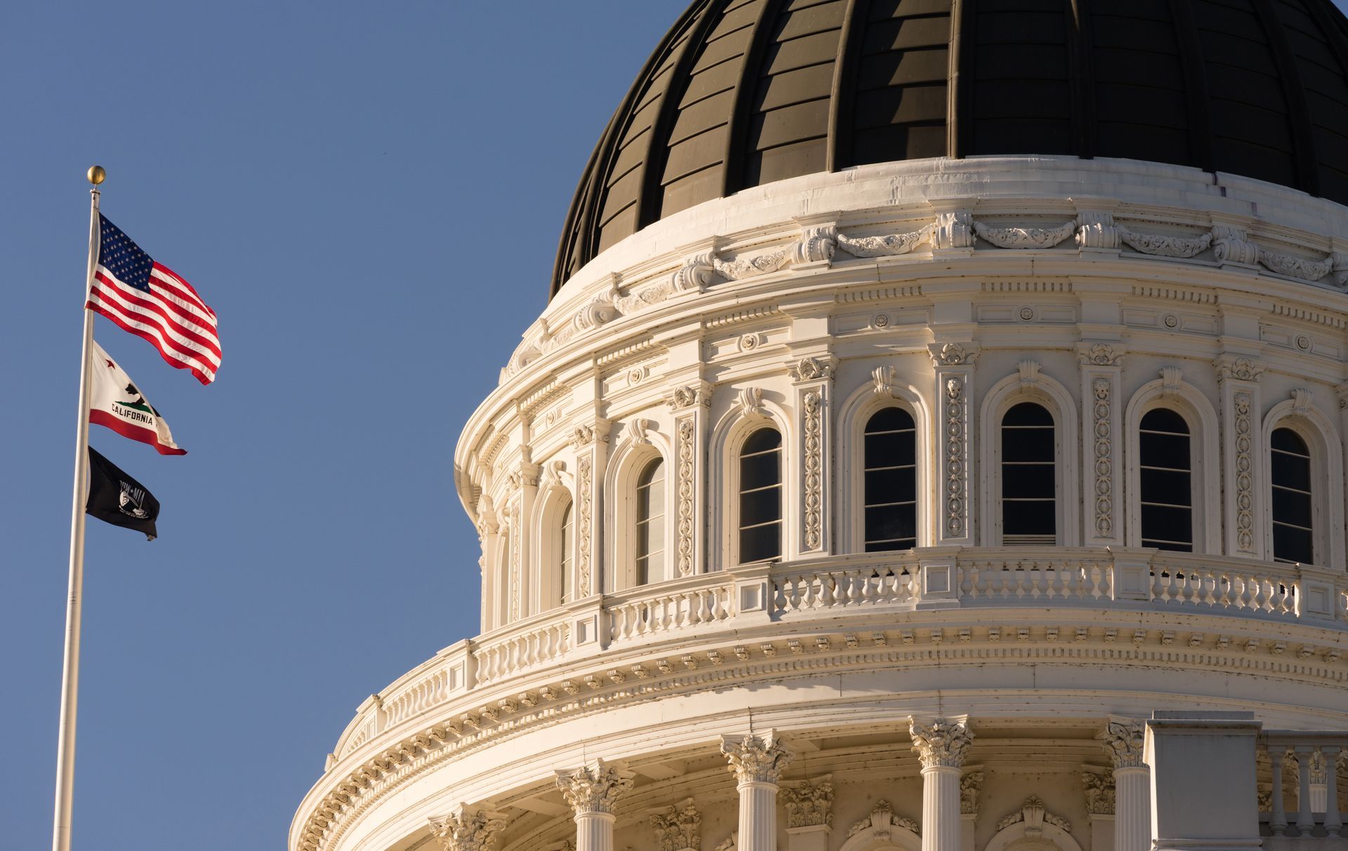 Three flags are flying in front of the capitol building