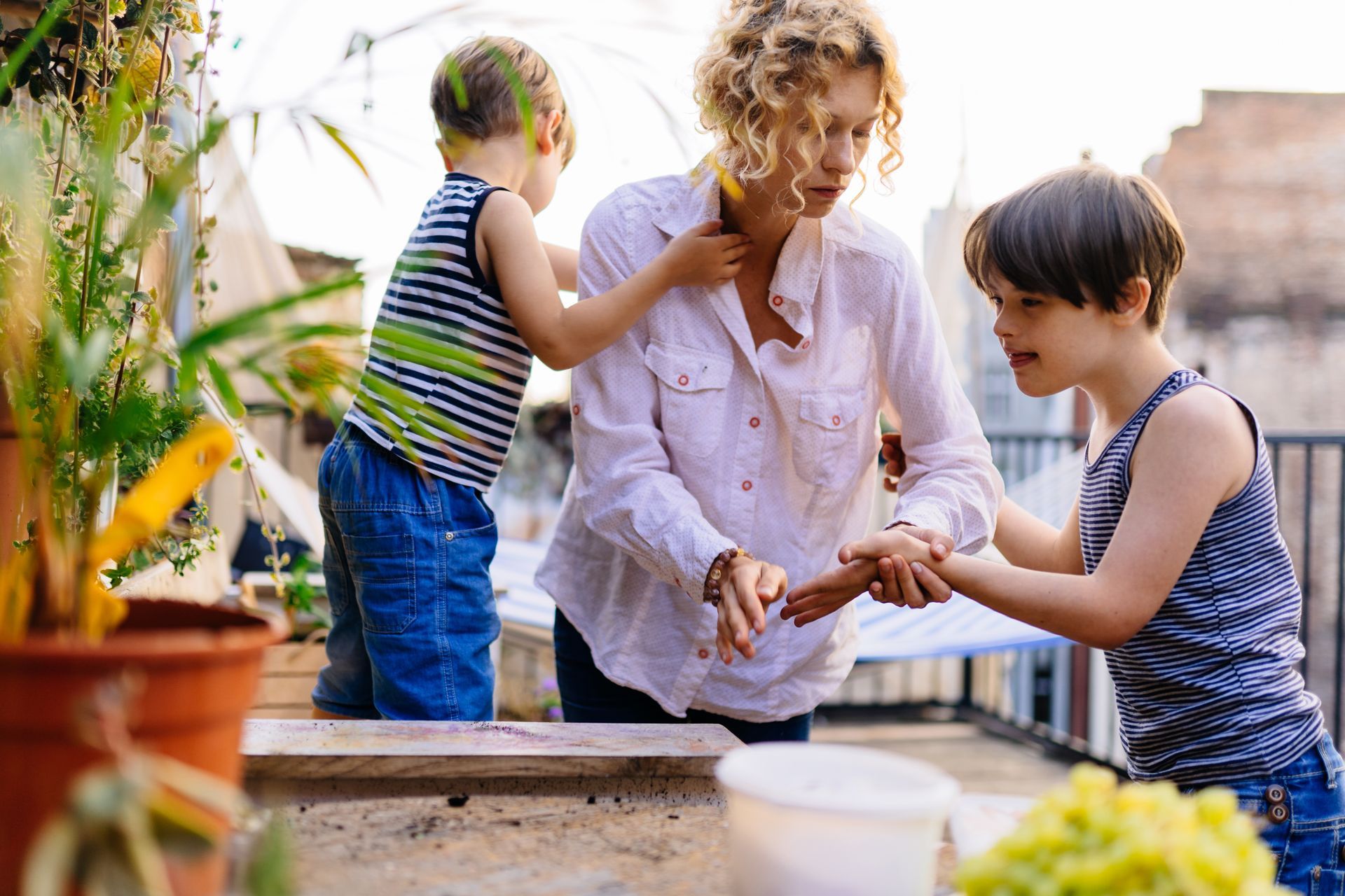 A woman and two children are playing with grapes on a balcony.