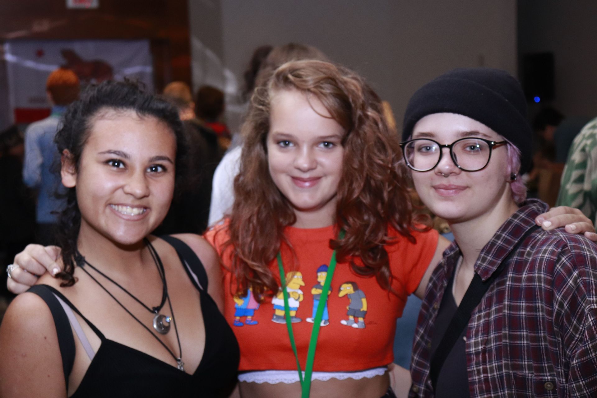 Three girls posing for a picture with one wearing a crop top with the simpsons on it