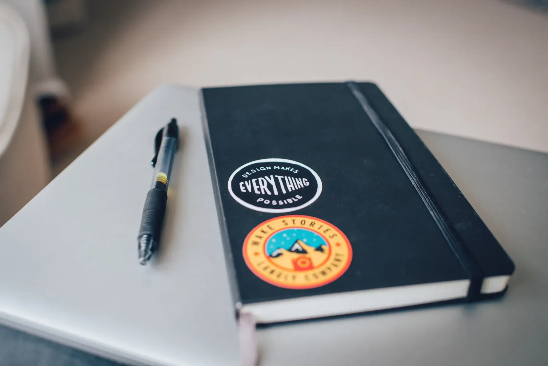 A notebook with stickers on it sits on a laptop next to a pen