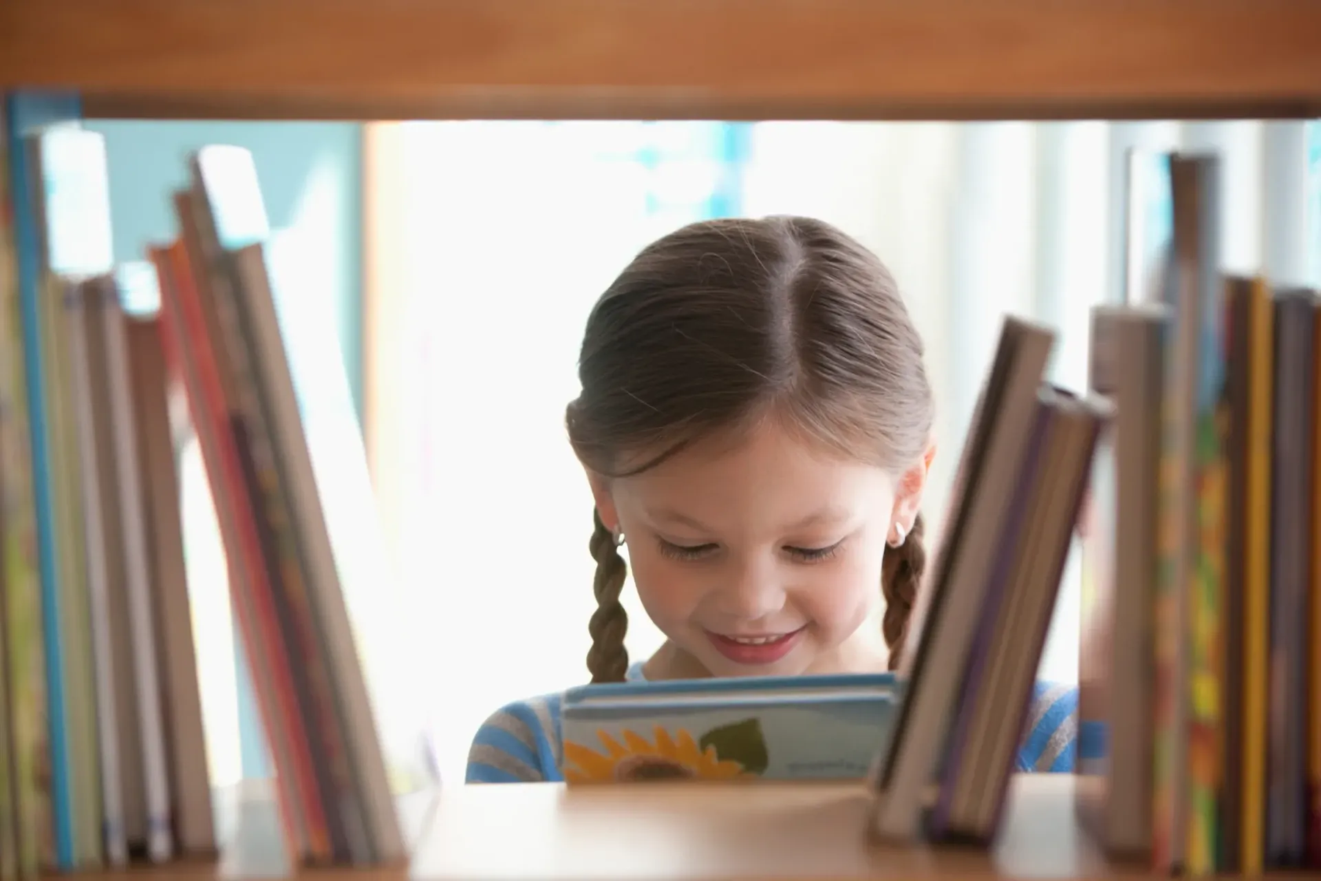 A little girl is reading a book in a library.