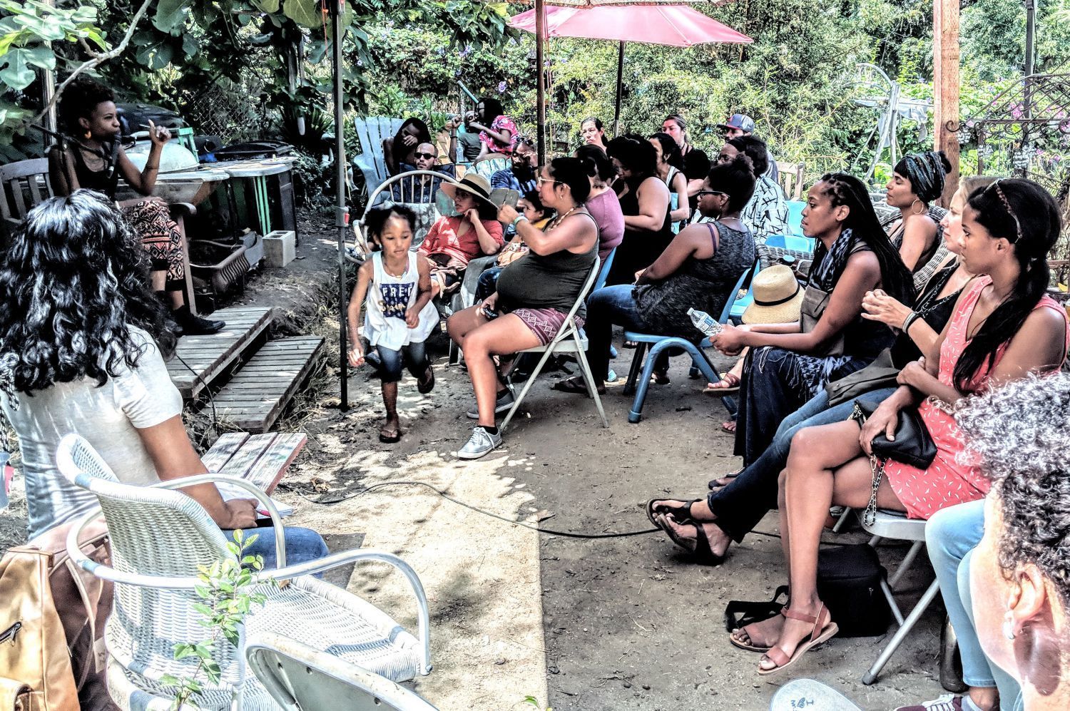 A group of people are sitting in chairs under an umbrella.