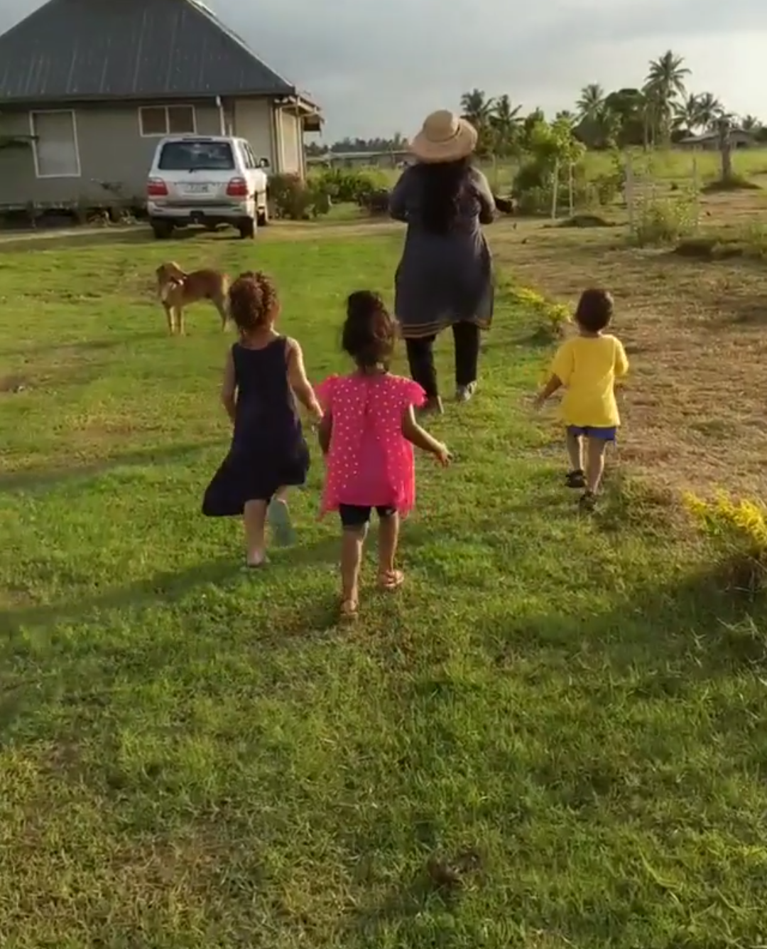 A woman and three children are running in a grassy field