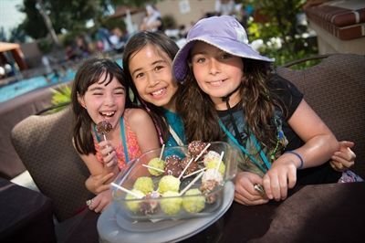 Three young girls are sitting at a table with a plate of food.