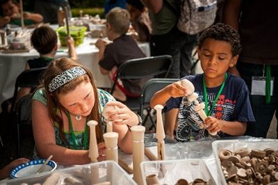 A boy and a girl are sitting at a table making wooden sculptures.