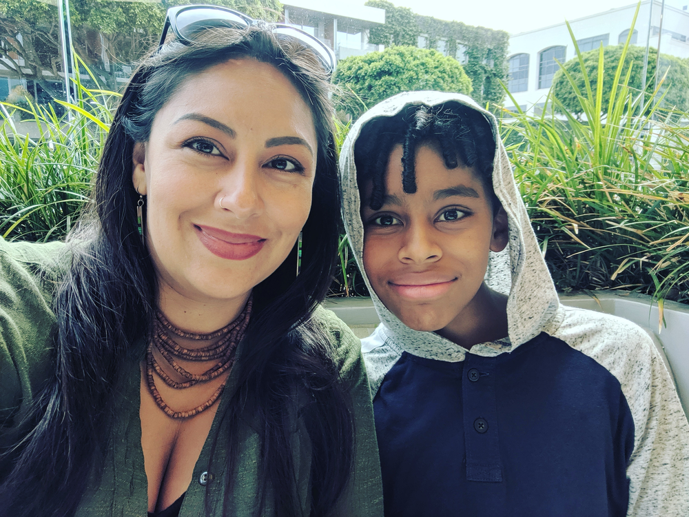 A woman and a boy are posing for a picture together . the boy is wearing a hoodie.