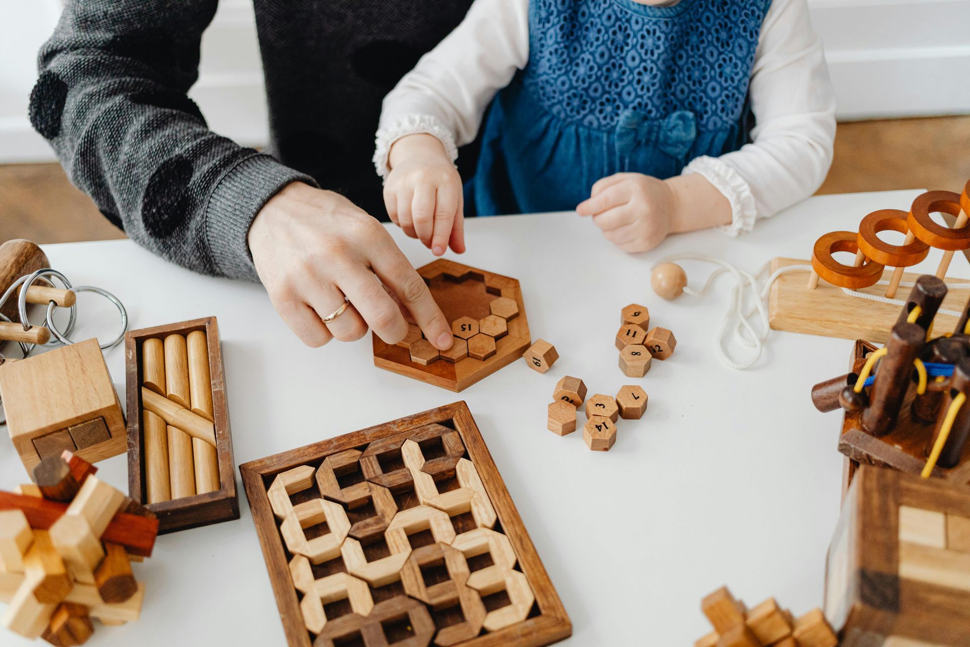 A man and a little girl are playing with wooden puzzles at a table.