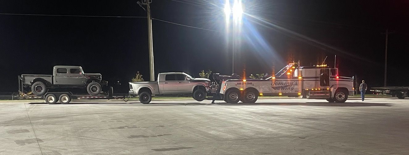 A row of tow trucks are parked in a parking lot at night.