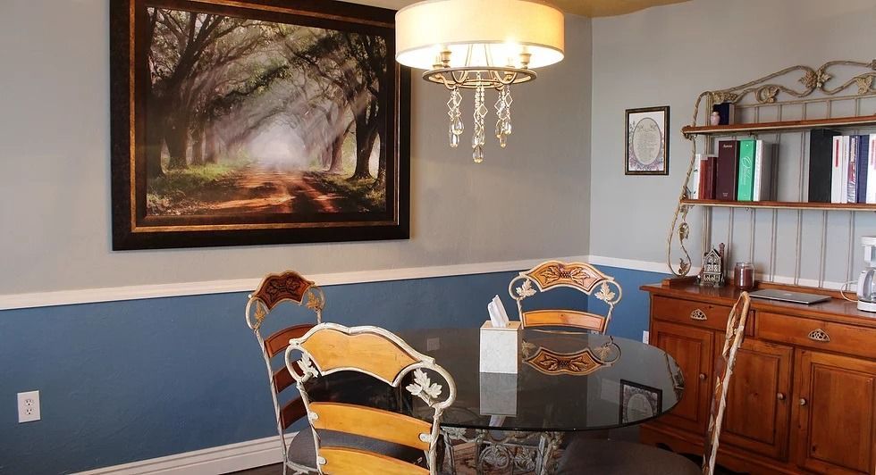 Dining room with a glass table, ornate chairs, and a landscape print on the blue and white wall.