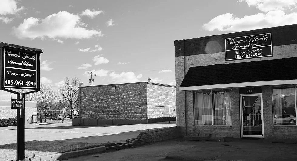 Black and white photo of Brewer Family Funeral Home building with signage and signpost on a sunny day.
