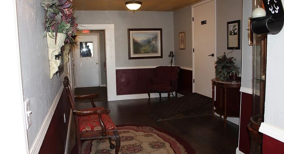 Hallway with dark wood floor, red accents, ornate chair, and painting. A grandfather clock is on the right.