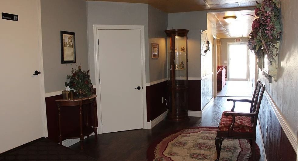 Hallway with dark wood floor, red wainscoting, gray walls, white door, grandfather clock, and a round rug.
