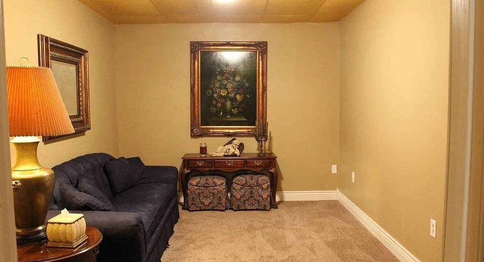 A small room with a sofa, side table with lamp, carpet, and artwork on the walls.