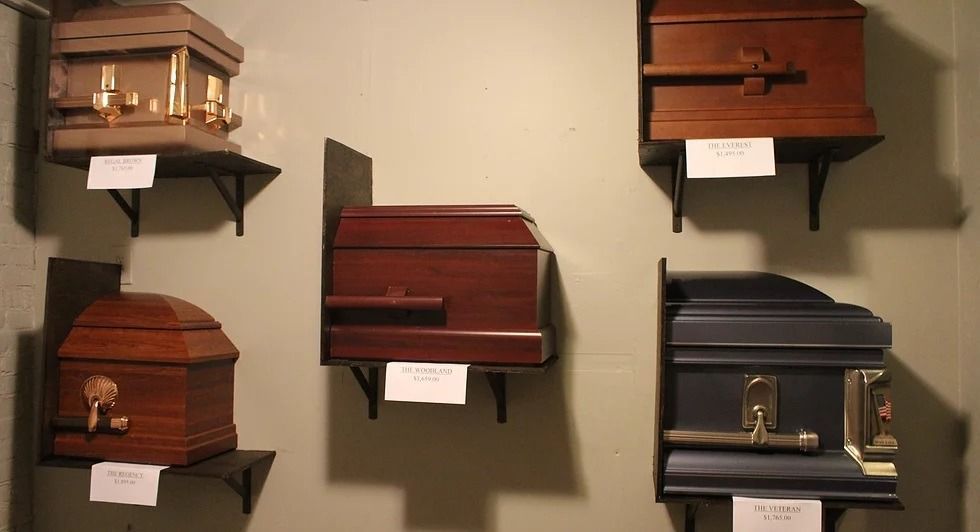 Caskets of varying wood tones and a black one on display shelves against a wall. Each has a small label.