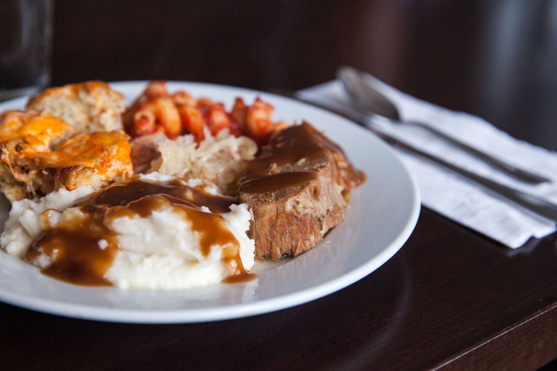 A plate of food with mashed potatoes , gravy , meat and vegetables on a table.