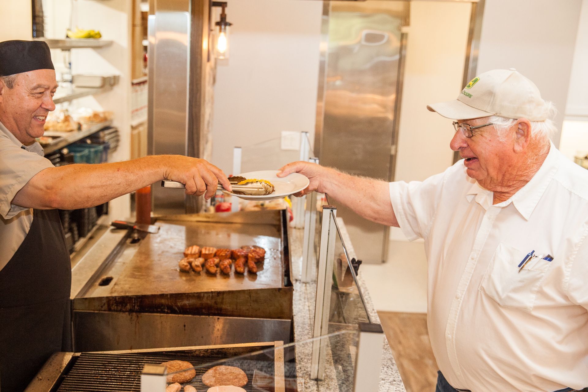 Two men are cooking food on a grill in a kitchen.