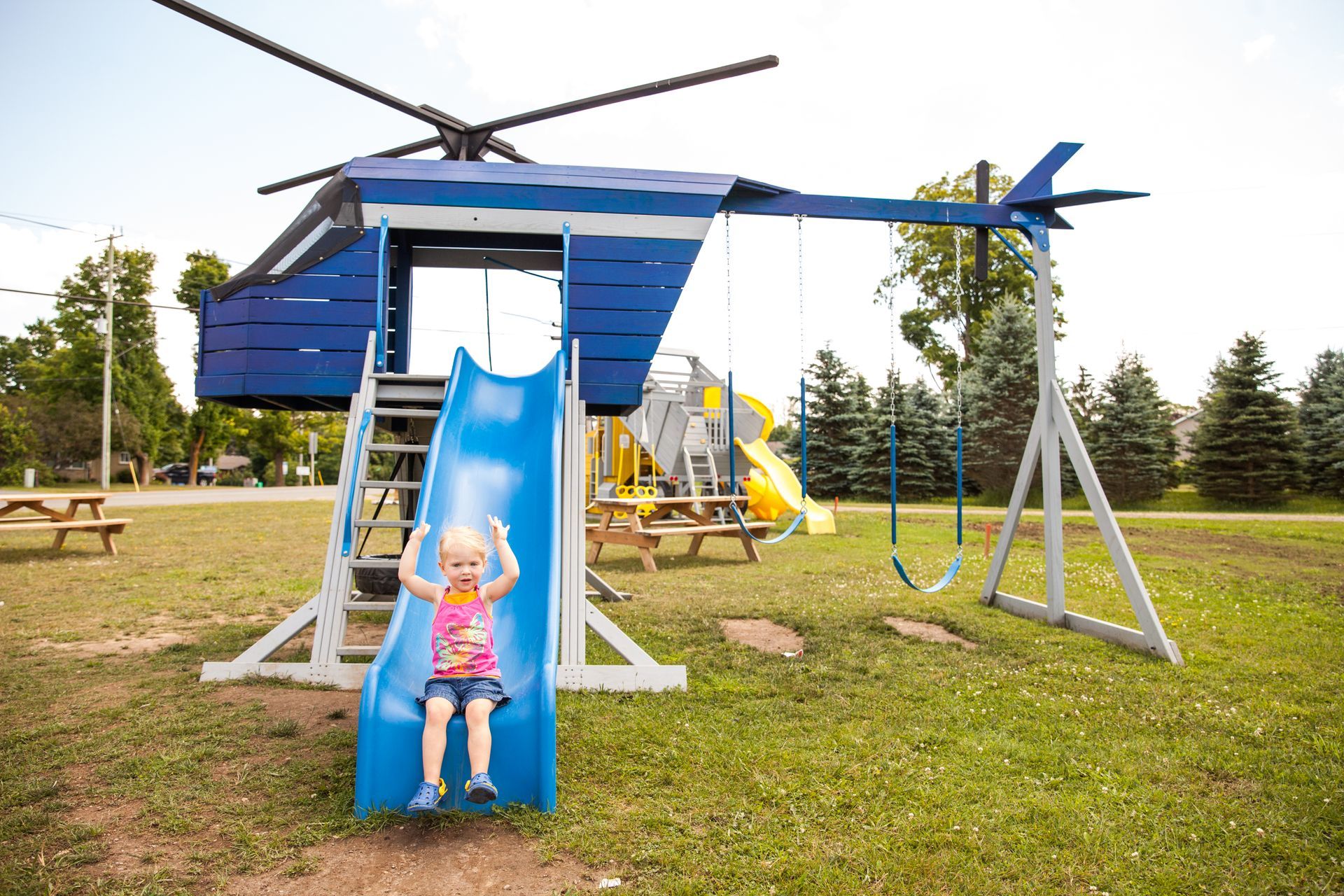 A little girl is sitting on a slide in a playground shaped like a helicopter.