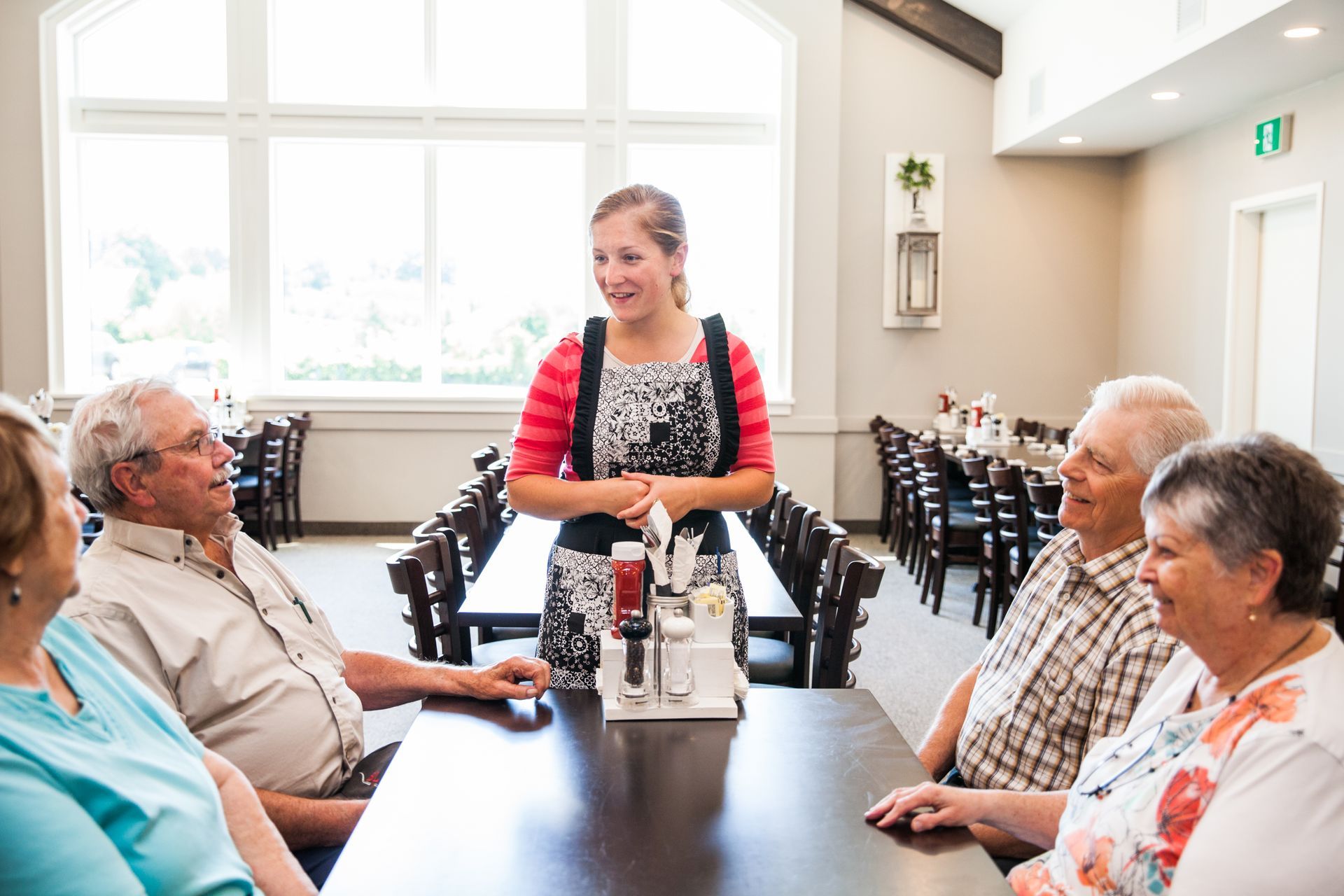 A group of people are sitting at a table in a restaurant talking to a waitress.