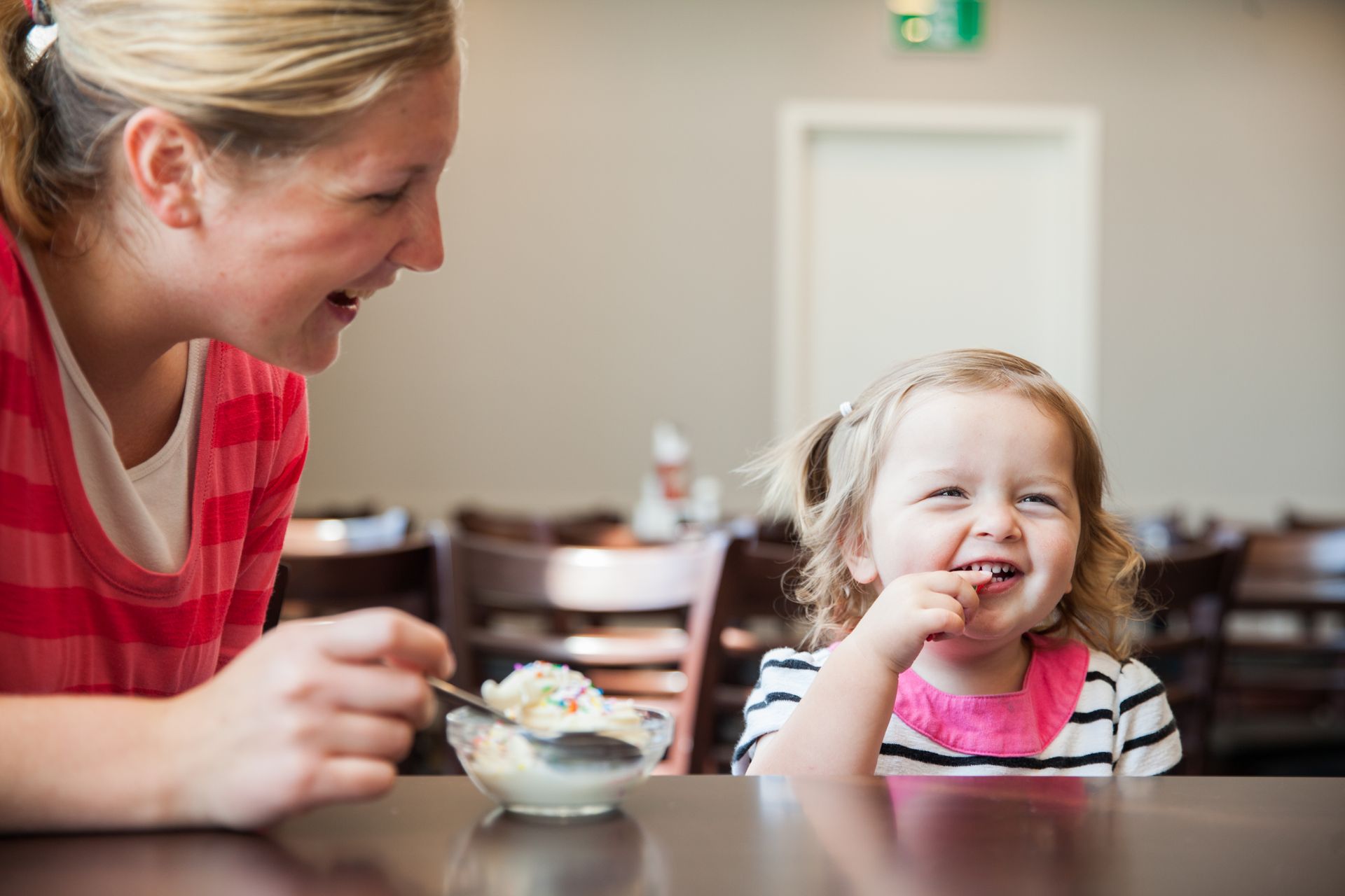 A woman and a little girl are sitting at a table eating ice cream.