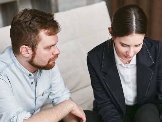 A man and a woman are sitting on a couch talking to each other.
