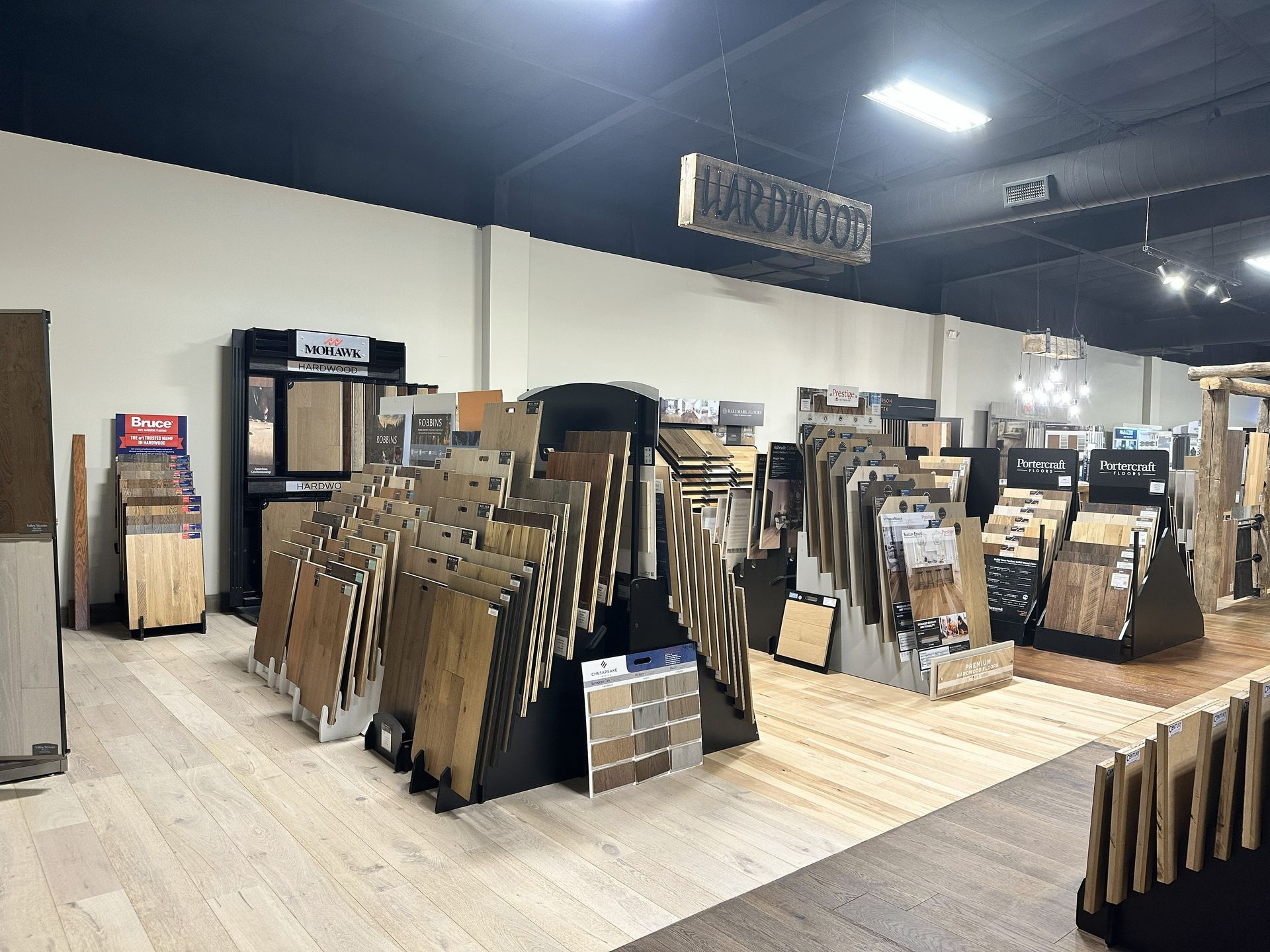 A showroom displays various wood and tile flooring samples arranged on racks with light-colored flooring on the floor.