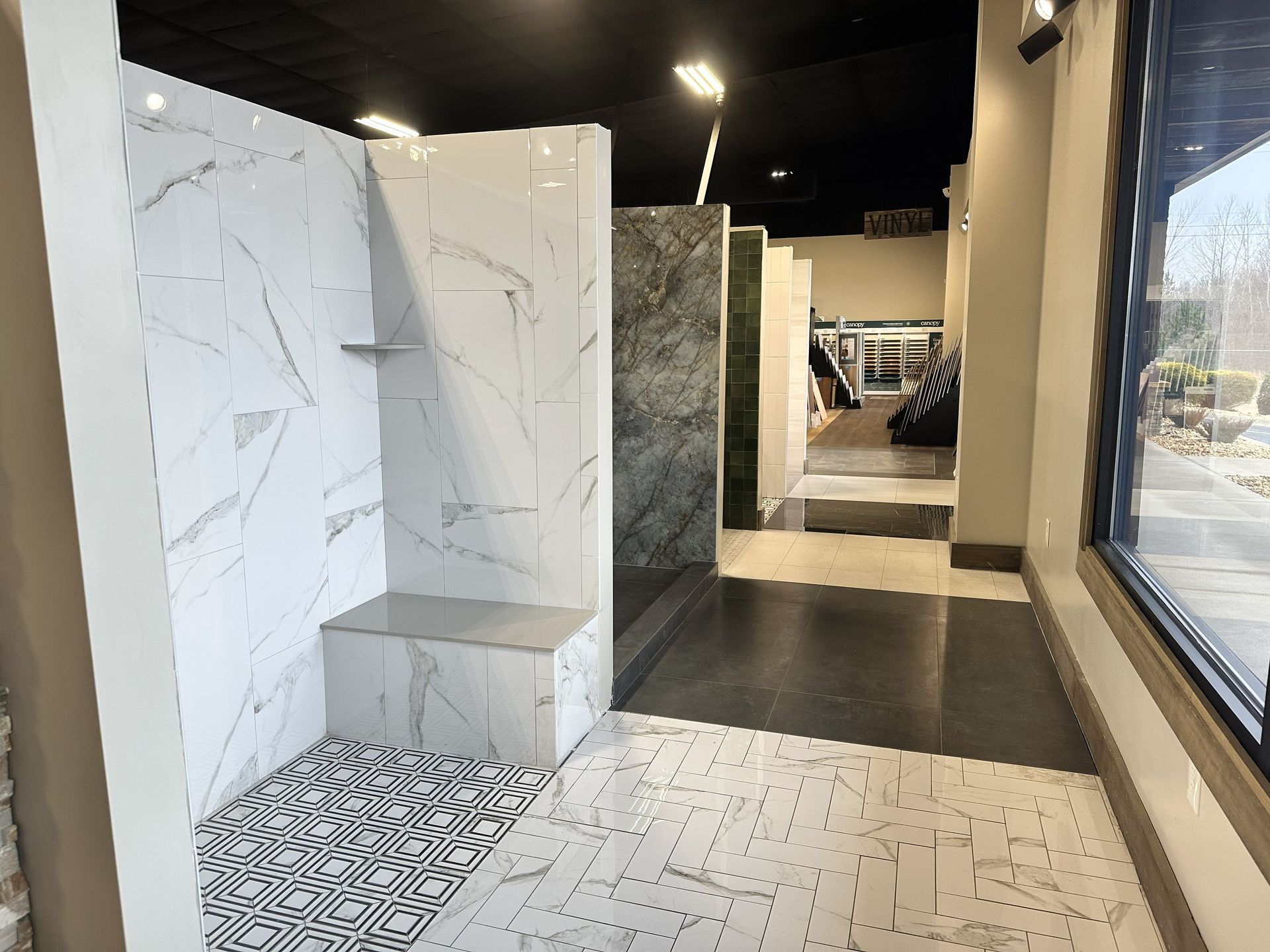 A showroom display featuring a marble-patterned shower stall with a built-in seat, geometric floor tiles, and open walkways.