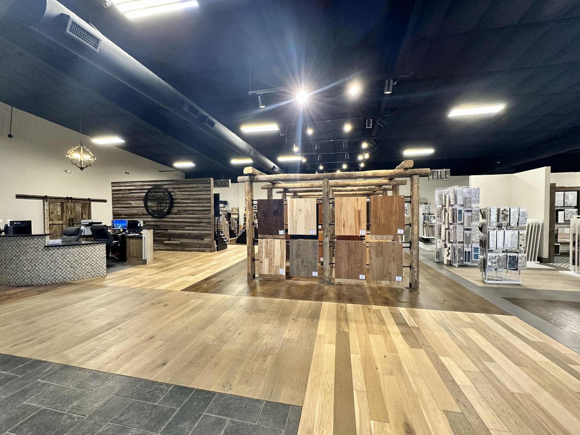 A showroom featuring various hardwood flooring samples on displays and floor sections, with a front reception desk.