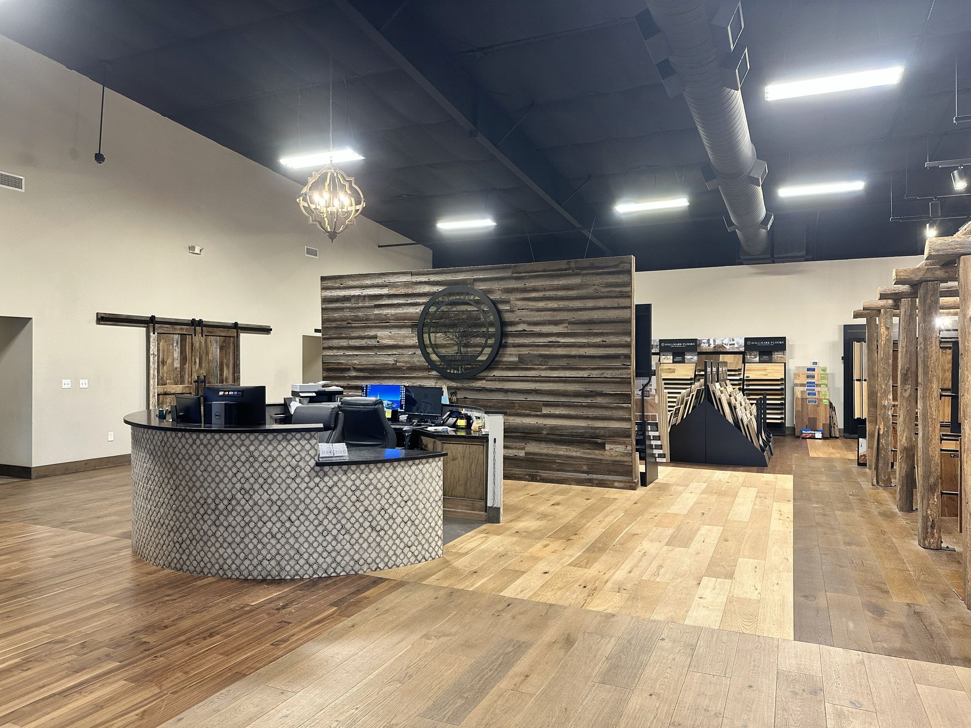 A curved stone reception desk in a rustic-style lobby with light wood floors, a dark accent wall, and exposed ductwork.