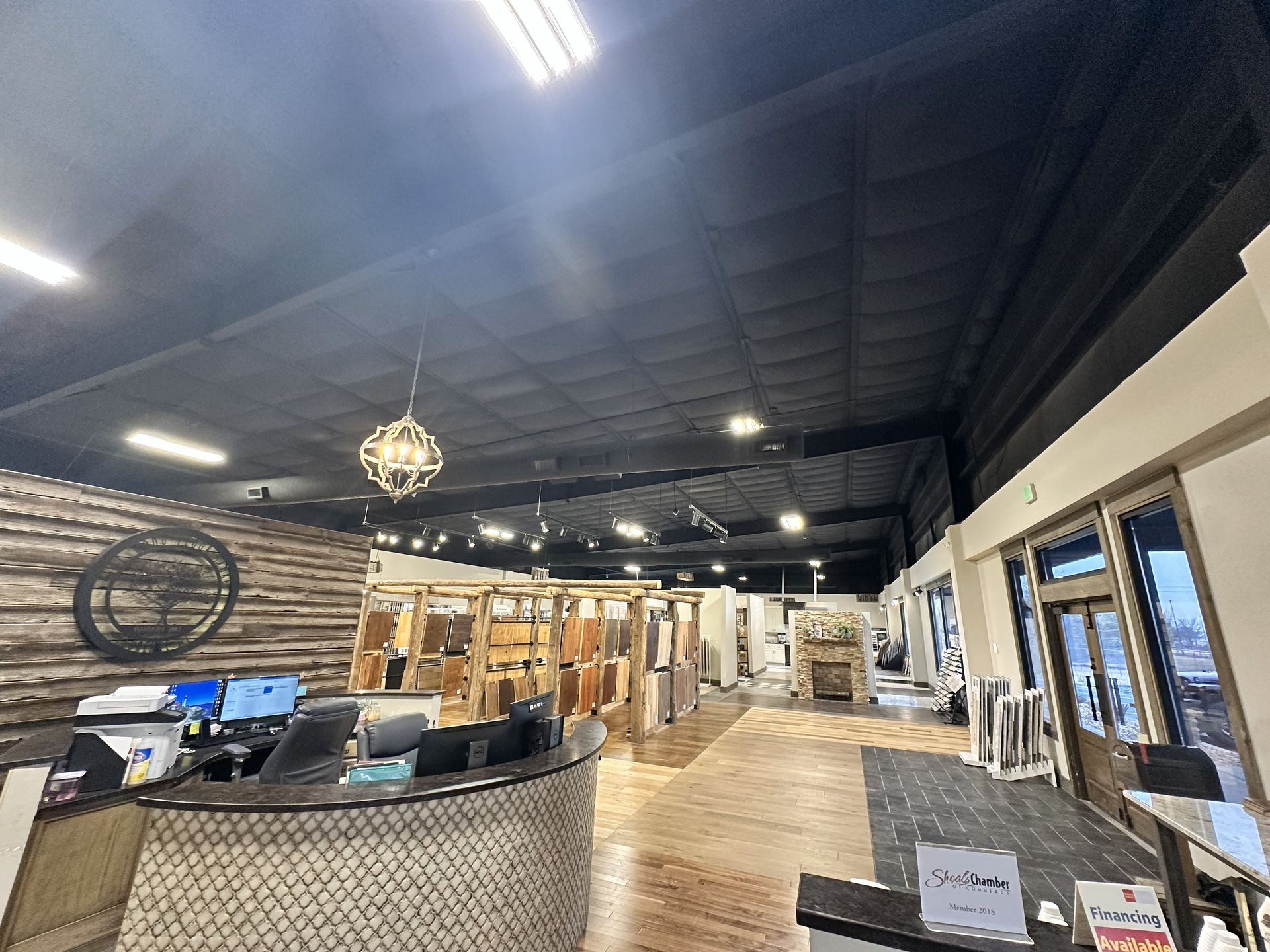 A spacious, modern showroom featuring a reception desk, wood-paneled wall, hanging light fixture, and displays of goods.