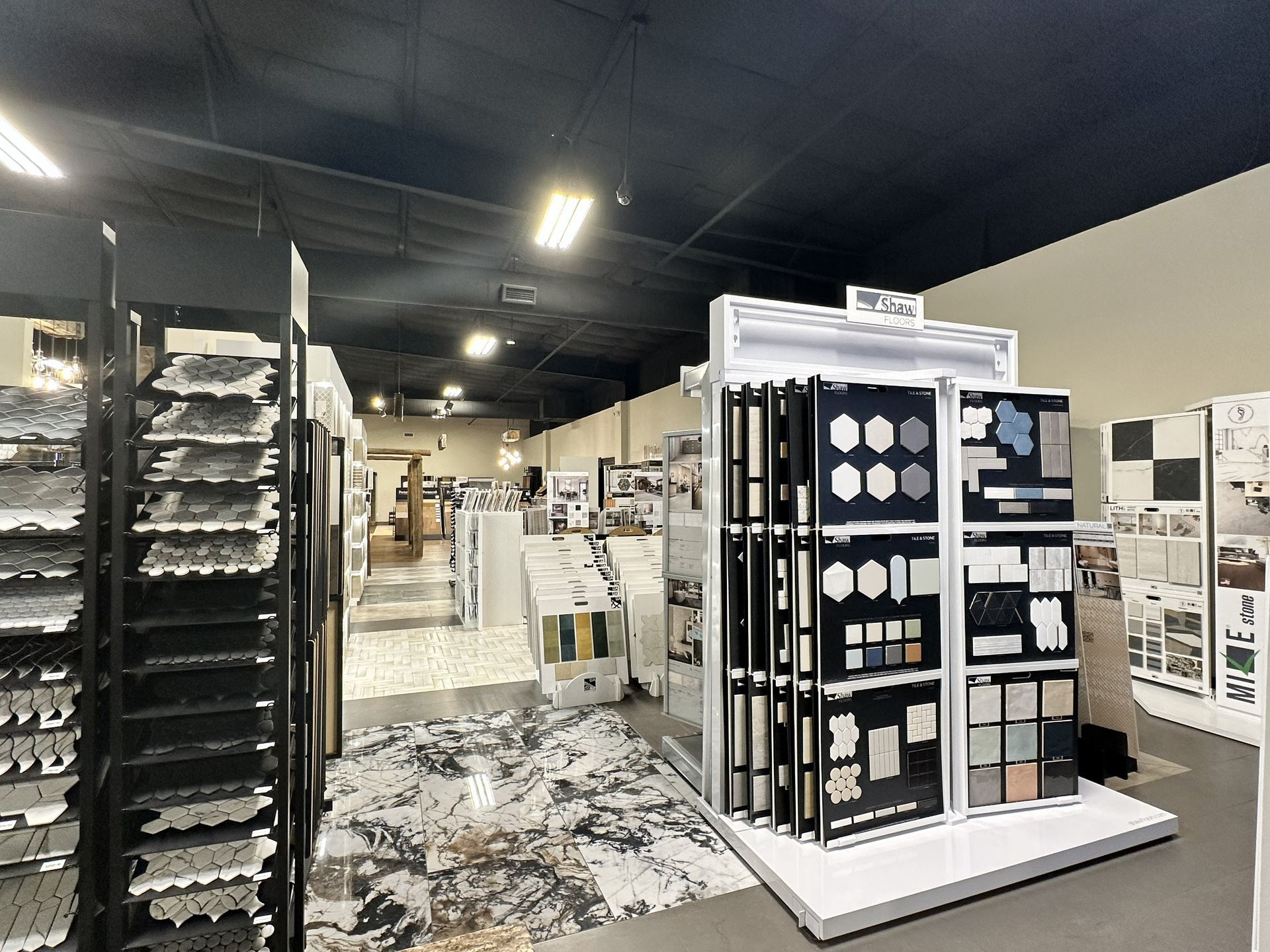 A tile showroom featuring displays with various samples, including hexagonal tiles, arranged on racks and floor displays.