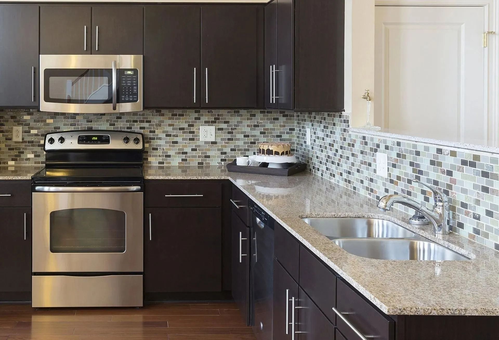 Modern kitchen with dark brown cabinetry, stainless steel appliances, granite countertops, and a mosaic tile backsplash.
