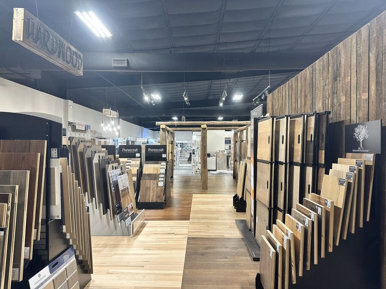A showroom interior displaying numerous wood flooring samples and planks on racks, with a central aisle.