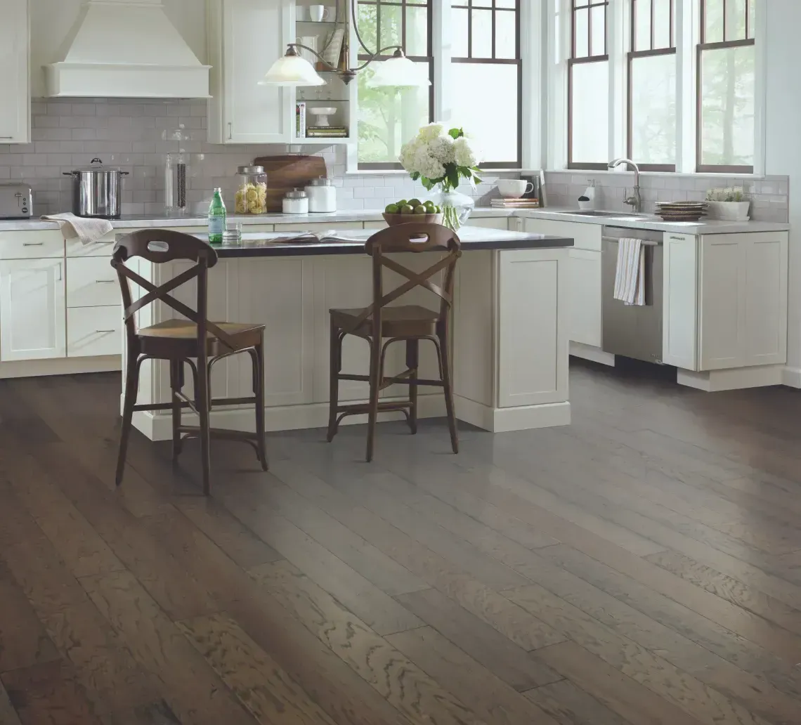 A bright, modern kitchen with white cabinets, a central island with two wooden stools, and dark hardwood flooring.