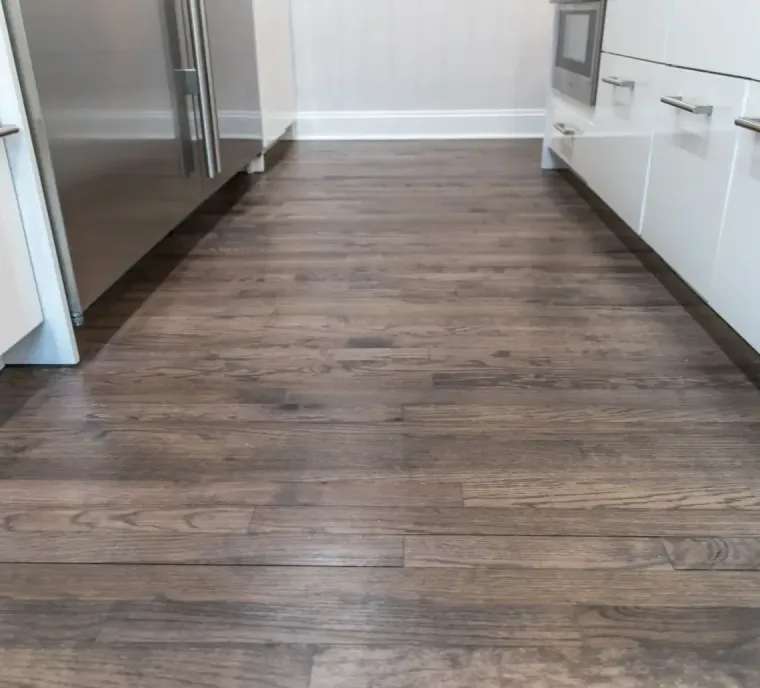 A narrow, wooden-floored kitchen corridor between white cabinets and a stainless steel appliance.