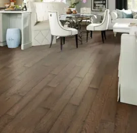 A bright, open-concept living area featuring rich brown hardwood flooring, a kitchen island, and white dining furniture.
