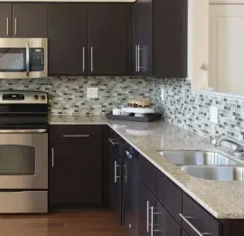 Modern kitchen with dark brown cabinetry, stainless steel appliances, granite countertops, and a mosaic tile backsplash.