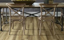 Two wooden cross-back chairs with woven seats positioned at a rustic dining table on a light wood-look floor.