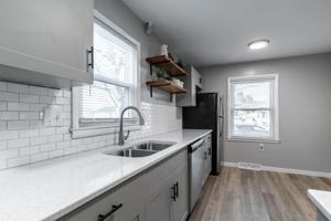 A modern kitchen featuring gray cabinets, white countertops, subway tile backsplash, a black refrigerator, and wood floors.