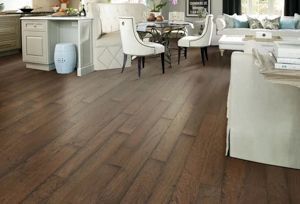 A bright, open-concept living area featuring rich brown hardwood flooring, white dining chairs, and neutral furniture.