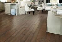 A bright, open-concept living area featuring rich brown hardwood flooring, white dining chairs, and neutral furniture.