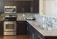 A modern kitchen with dark brown cabinets, granite countertops, a stainless steel oven, and a tiled backsplash.