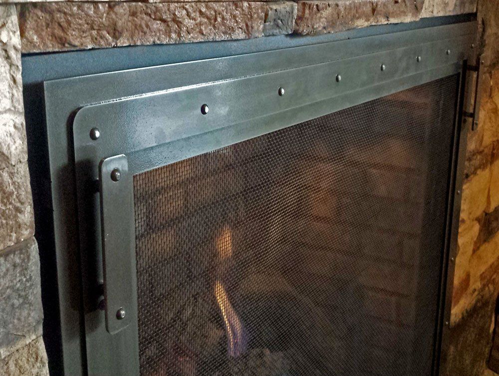 Close-up of a fireplace with a dark metal screen. The screen is in front of a brick interior.