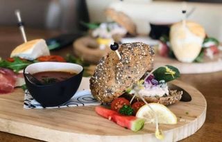 Gourmet sliders geserveerd op een ronde houten plank met een klein kommetje soep, cherrytomaatjes en een schijfje citroen.